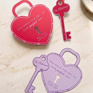 May include: Heart-shaped wedding invitation cards in red and lavender, with key-shaped tags. The cards read "You hold the key to our perfect day" and "Will you join us?" with a keyhole design. The key tags have the names "The Robinsons" and the date.