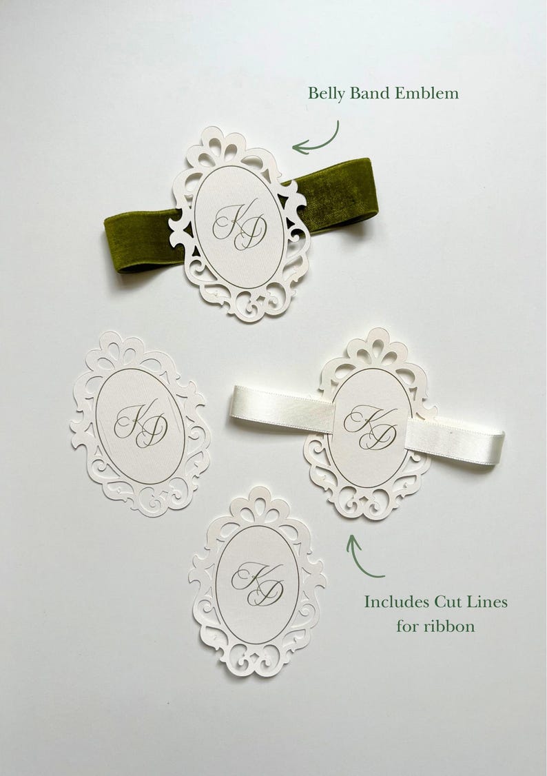 May include: Four white oval paper emblems with intricate die-cut borders and the monogram KD in script. One emblem features a green velvet ribbon, another a white satin ribbon, and two are plain. Text labels read Belly Band Emblem and Includes Cut Lines for ribbon.
