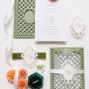 May include: A wedding invitation suite featuring sage green laser-cut cardstock folders, white cards with black text, a dark green velvet ring box, a thin diamond band, white ribbon, and peach-colored dahlia flowers. The text includes names Kaitlin Macdonald and David Johnson, the date 24th September 2026, and The Beverly Manor.