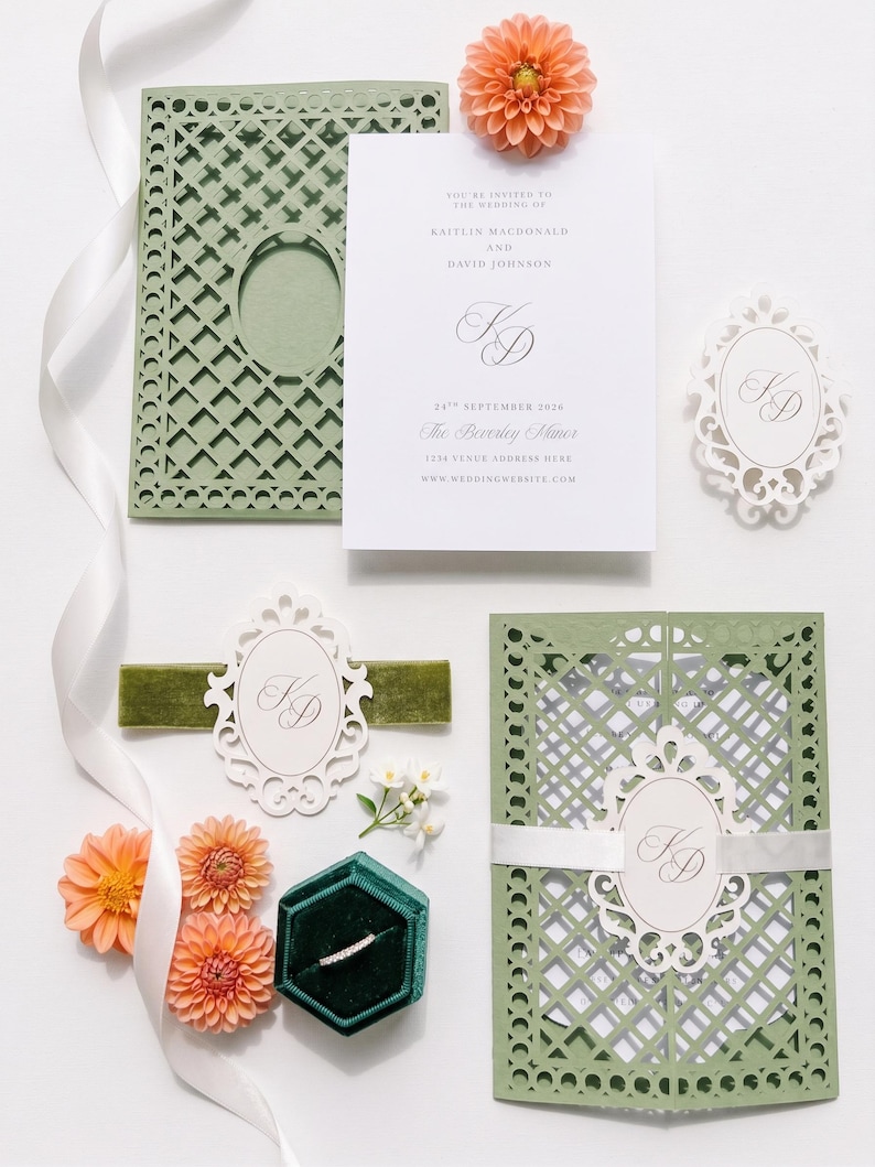 May include: A wedding invitation suite featuring sage green laser-cut cardstock folders, white cards with black text, a dark green velvet ring box, a thin diamond band, white ribbon, and peach-colored dahlia flowers. The text includes names Kaitlin Macdonald and David Johnson, the date 24th September 2026, and The Beverly Manor.