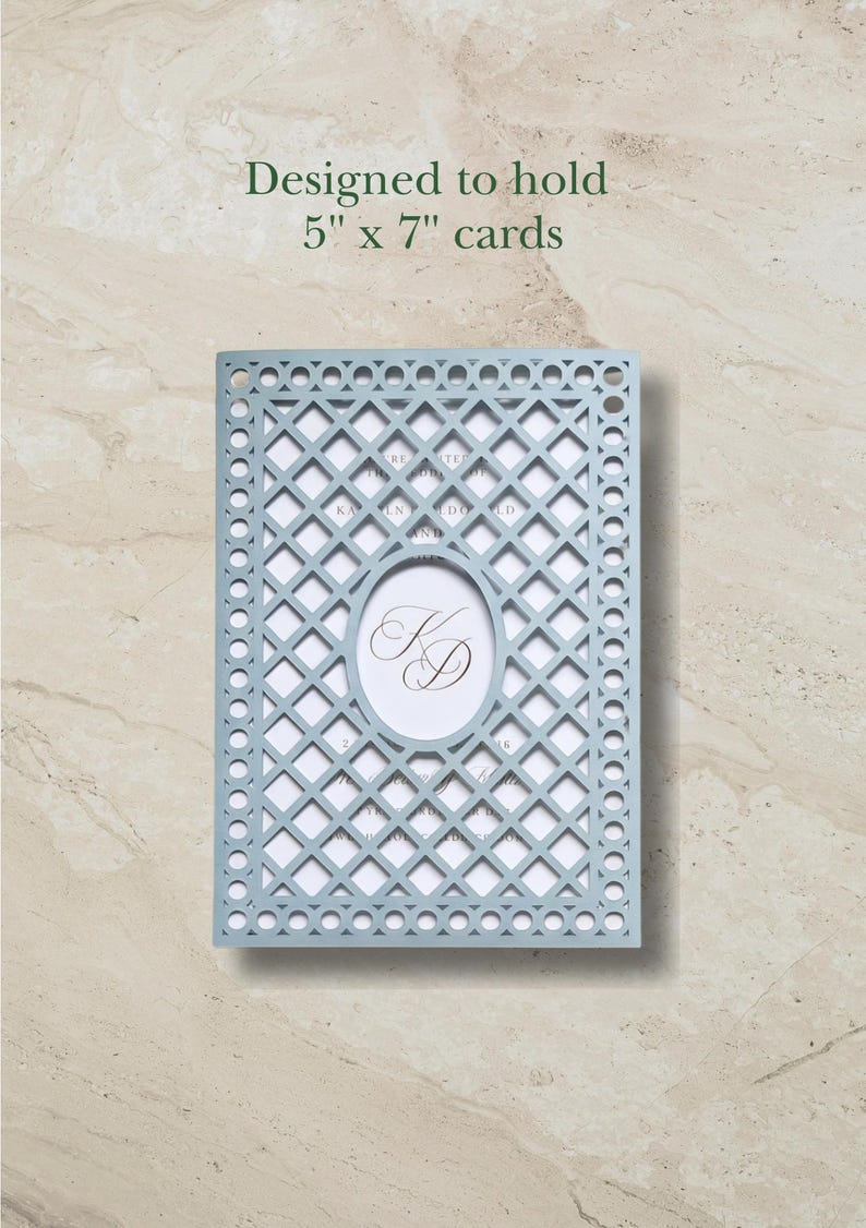 May include: A light blue laser-cut card holder with a lattice pattern and a central oval cutout featuring the monogram KD. The holder is designed to hold 5" x 7" cards. The intricate geometric design includes circular accents along the border.