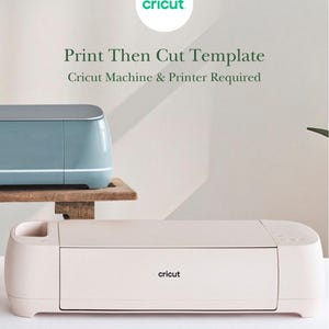 May include: A light pink Cricut cutting machine sits in the foreground, while a blue Cricut machine is partially visible on a wooden shelf behind it. The text reads: "cricut", "Print Then Cut Template", and "Cricut Machine & Printer Required".