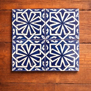 May include: Four square ceramic tiles with a blue and white geometric starburst pattern. The tiles are arranged on a wooden surface, creating a decorative design. The blue and white color scheme provides a striking contrast.