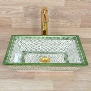 Op de afbeelding: Een rechthoekige keramische wastafel met een groen en wit patroon, met een gouden kraan en afvoer. De wastafel heeft een decoratief ontwerp en is waarschijnlijk voor een badkamer.