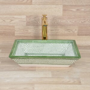 K&ouml;nnte beinhalten: Rechteckiges Keramik-Waschbecken mit gr&uuml;n-wei&szlig;em Muster. Das Waschbecken hat einen goldenen Wasserhahn und einen dekorativen Rand. Eine einzigartige Erg&auml;nzung f&uuml;r jedes Badezimmer.