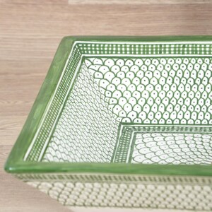 K&ouml;nnte beinhalten: Eine quadratische Servierschale aus Keramik mit gr&uuml;nem Rand und einem wei&szlig;en und gr&uuml;nen Punktmuster. Die Schale hat ein geometrisches Design und wird wahrscheinlich zum Servieren von Speisen oder als dekoratives St&uuml;ck verwendet.