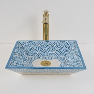 Op de afbeelding: Een rechthoekige keramische badkamer wastafel met een blauw en wit paisley design. De wastafel heeft een gouden kraan en een gouden afvoer. De wastafel is een opzet wastafel, ontworpen om op een wastafelblad te staan.