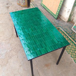 Peut inclure: Une table rectangulaire avec un dessus carrelé vert vif et des pieds en métal noir. La surface de la table est composée de petits carreaux rectangulaires, créant un aspect texturé. La table mesure environ 152 cm de long et 76 cm de large.