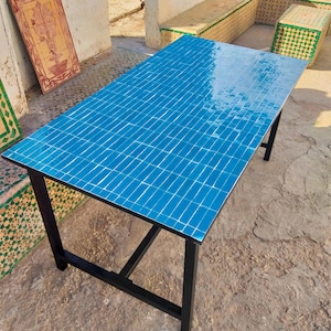 May include: A rectangular table with a vibrant blue tiled top and a black metal frame. The tabletop is composed of small, square tiles, creating a mosaic effect. The table's legs are straight and sturdy, providing a minimalist design.