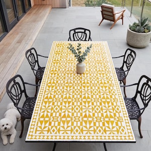 May include: An outdoor dining table with a yellow and white geometric pattern, surrounded by six black metal chairs. A small white dog is lying on the ground near the table. A vase with greenery sits in the center of the table.