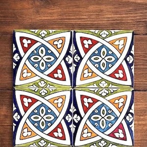 May include: Four square ceramic tiles with a colorful geometric design. Each tile features a central blue flower-like pattern, surrounded by red, yellow, green, and white accents, set against a dark blue border. The tiles are arranged on a wooden surface.