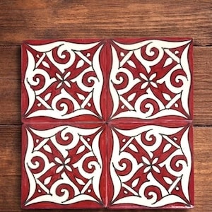 Pode incluir: Quatro azulejos quadrados de cerâmica com um padrão geométrico vermelho e branco repetitivo. O design apresenta linhas giratórias e formas simétricas, com contornos pretos. Os azulejos estão dispostos sobre uma superfície de madeira.