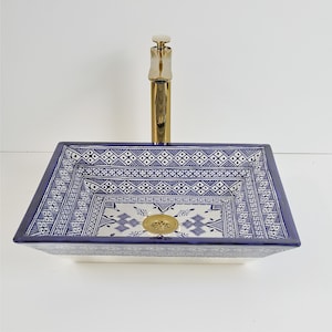 May include: A square ceramic sink with a blue and white geometric pattern. The sink has a gold faucet and drain. The sink is a decorative bathroom fixture.
