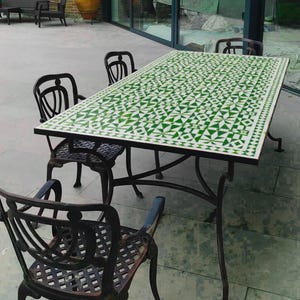 May include: An outdoor dining set comprising a rectangular table with a green and white geometric tiled surface. The table, supported by a black metal frame, is surrounded by four black metal chairs. The set is designed for outdoor use, ideal for a patio or garden.