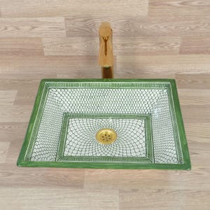 K&ouml;nnte beinhalten: Ein rechteckiges Waschbecken mit gr&uuml;nem und wei&szlig;em Muster und einer goldenen Armatur. Das Waschbecken hat ein dekoratives Design mit einem gr&uuml;nen Rand und einem wei&szlig;en Innenraum mit sich wiederholendem Muster. Die Armatur ist goldfarben.