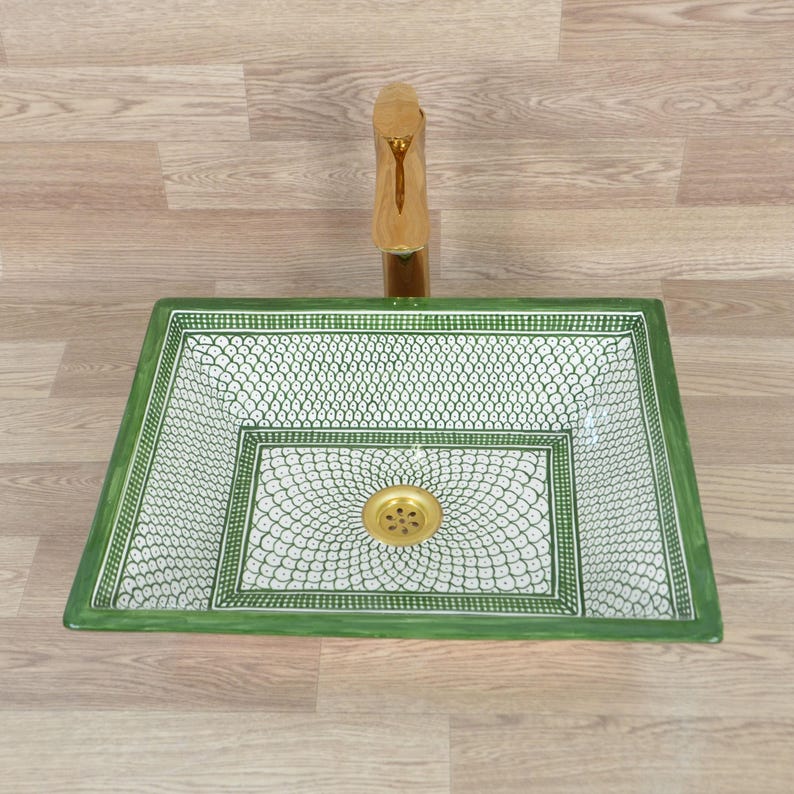 K&ouml;nnte beinhalten: Ein rechteckiges Waschbecken mit gr&uuml;nem und wei&szlig;em Muster und einer goldenen Armatur. Das Waschbecken hat ein dekoratives Design mit einem gr&uuml;nen Rand und einem wei&szlig;en Innenraum mit sich wiederholendem Muster. Die Armatur ist goldfarben.