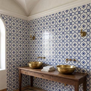 May include: A bathroom with blue and white patterned tile walls. Two brass sinks sit atop a wooden vanity. The sinks have brass faucets. A stack of folded white towels is on the vanity between the sinks. The room has a white arched ceiling.