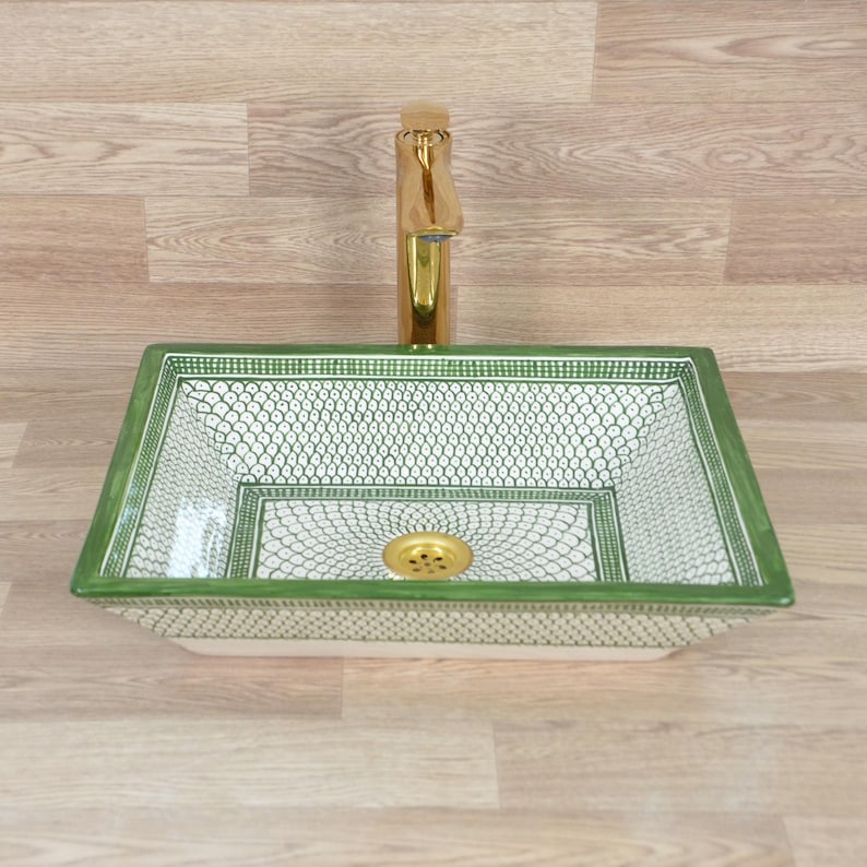 May include: A rectangular ceramic sink with a green and white pattern, featuring a gold faucet and drain. The sink has a decorative design and is likely for a bathroom.