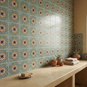 May include: A bathroom with patterned tiles in teal, yellow, and burgundy, featuring a starburst design. A concrete countertop holds potted plants, folded towels, and a bar of soap. The tiles are approximately 20 cm x 20 cm.