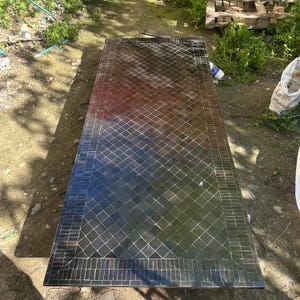 May include: Rectangular mosaic tile table with a dark, reflective surface. The table features a diamond pattern in shades of black, brown, and blue. The border is made of rectangular tiles. The table is approximately 183 cm long.