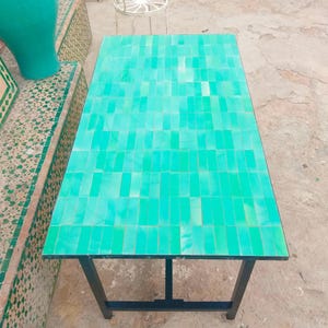 May include: A rectangular table with a mosaic tile top in shades of turquoise and green. The tiles are arranged in a brick pattern. The table has a black metal frame and legs.