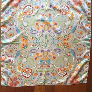 May include: A square, beige silk scarf with a floral pattern in shades of orange, yellow, green, blue, and purple. The pattern is symmetrical and features a variety of flowers and leaves.