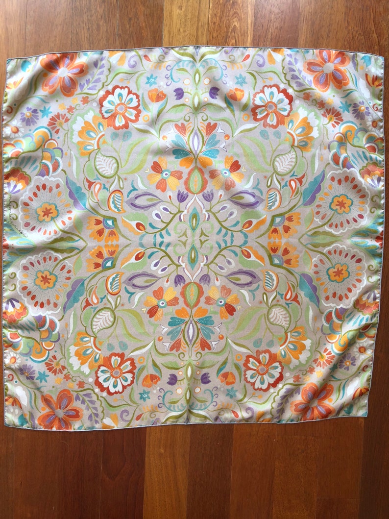 May include: A square, beige silk scarf with a floral pattern in shades of orange, yellow, green, blue, and purple. The pattern is symmetrical and features a variety of flowers and leaves.