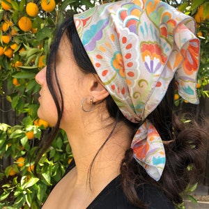 May include: A person with long dark hair wearing a colorful paisley bandana tied around their head. The bandana has a light background with orange, blue, green, and purple floral patterns.