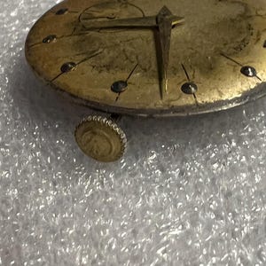 K&ouml;nnte beinhalten: Nahaufnahme eines Vintage-Zifferblatts mit goldfarbenem Finish. Die Uhr hat schwarze Stundenmarkierungen, goldene Zeiger und eine kleine Krone. Das Zifferblatt hat ein abgenutztes, antikes Aussehen.