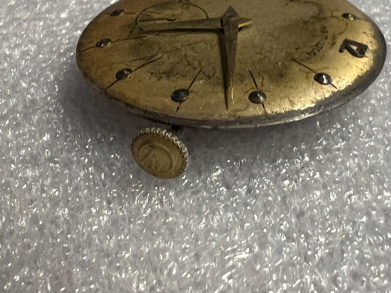 K&ouml;nnte beinhalten: Nahaufnahme eines Vintage-Zifferblatts mit goldfarbenem Finish. Die Uhr hat schwarze Stundenmarkierungen, goldene Zeiger und eine kleine Krone. Das Zifferblatt hat ein abgenutztes, antikes Aussehen.