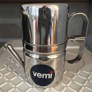May include: A stainless steel coffee maker with a handle and a spout. The coffee maker has a black and white logo that says "vemi". The coffee maker is sitting on a white surface.