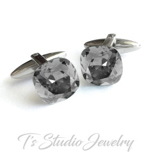 May include: A pair of silver cufflinks with a square, dark gray crystal stone on each cufflink.