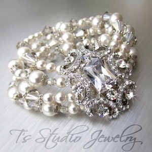 May include: A multi-strand bracelet featuring white pearls, clear crystals, and a large, clear, rectangular rhinestone centrepiece set in a silver-toned metal frame.