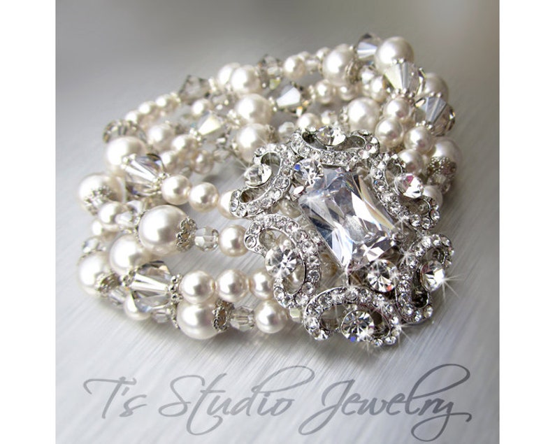 May include: A multi-strand bracelet featuring white pearls, clear crystals, and a large, clear, rectangular rhinestone centrepiece set in a silver-toned metal frame.