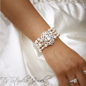 May include: A silver and white crystal and pearl bracelet with a large, ornate, crystal centrepiece. The bracelet is worn on a person's wrist.