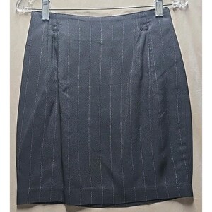 May include: A dark gray skirt with vertical silver pinstripes. The skirt is hanging on a metal hanger. The skirt has a straight cut and a simple design, suitable for business or casual wear.