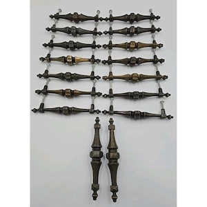 May include: A collection of antique bronze cabinet pulls and two matching decorative finials. The pulls have a detailed, ornate design with a central barrel shape and are attached with screws. The finials are elongated and feature similar detailing.