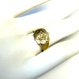 May include: A gold ring with a detailed floral design. The center of the ring features a flower with a white center and gold petals.