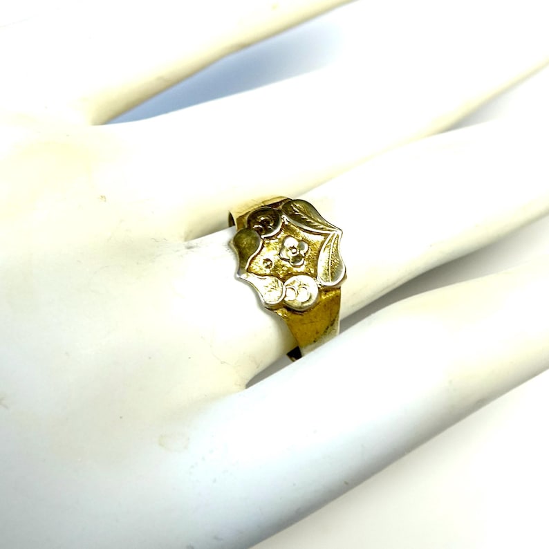 May include: A gold ring with a detailed floral design. The center of the ring features a flower with a white center and gold petals.