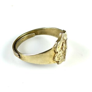 May include: A gold-toned ring with an intricate design on the band. The design features a floral motif with a raised center.