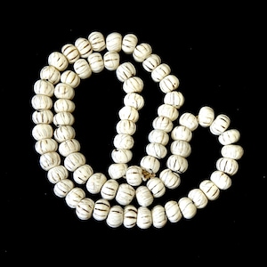 May include: A white beaded necklace with a striped pattern. The beads are round and have a smooth texture.