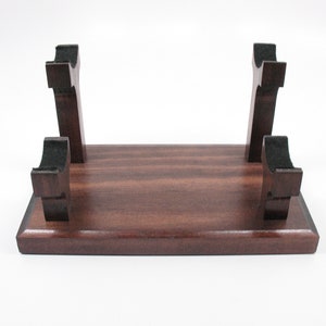 May include: A dark brown wooden stand with four upright supports. The supports have a curved design and are spaced evenly across the rectangular base. The stand is likely for displaying an item.