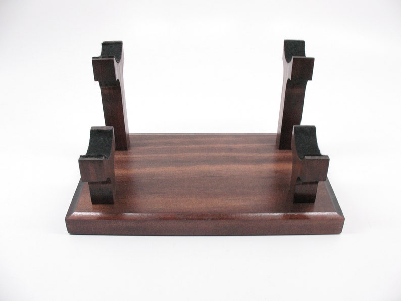 May include: A dark brown wooden stand with four upright supports. The supports have a curved design and are spaced evenly across the rectangular base. The stand is likely for displaying an item.