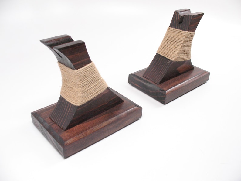 May include: Two dark stained wooden display stands. Each stand has a rectangular base and a curved top, wrapped with natural twine. The stands are designed to hold an item, likely a small decorative object.