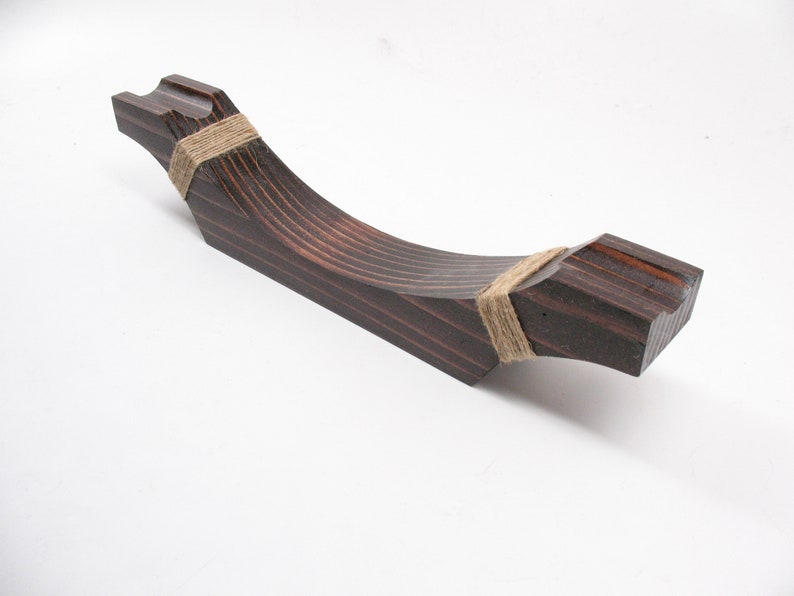 May include: A dark stained wooden handle with a curved design. The handle is wrapped with twine at both ends. The wood grain is visible, and the handle is set against a white background.