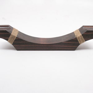 May include: A dark brown wooden decorative piece with a curved design. The piece is made of layered wood and is wrapped with twine at each end. The item is designed to hold an object.