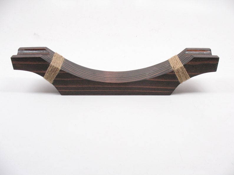 May include: A dark brown wooden decorative piece with a curved design. The piece is made of layered wood and is wrapped with twine at each end. The item is designed to hold an object.