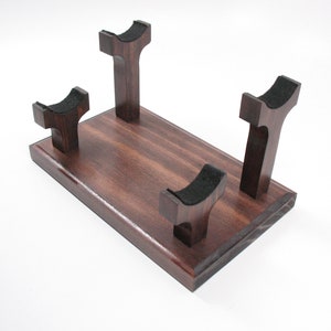 May include: A wooden display stand with a rectangular base and four upright supports. The supports have a curved top with black felt padding. The wood has a rich, dark brown finish.