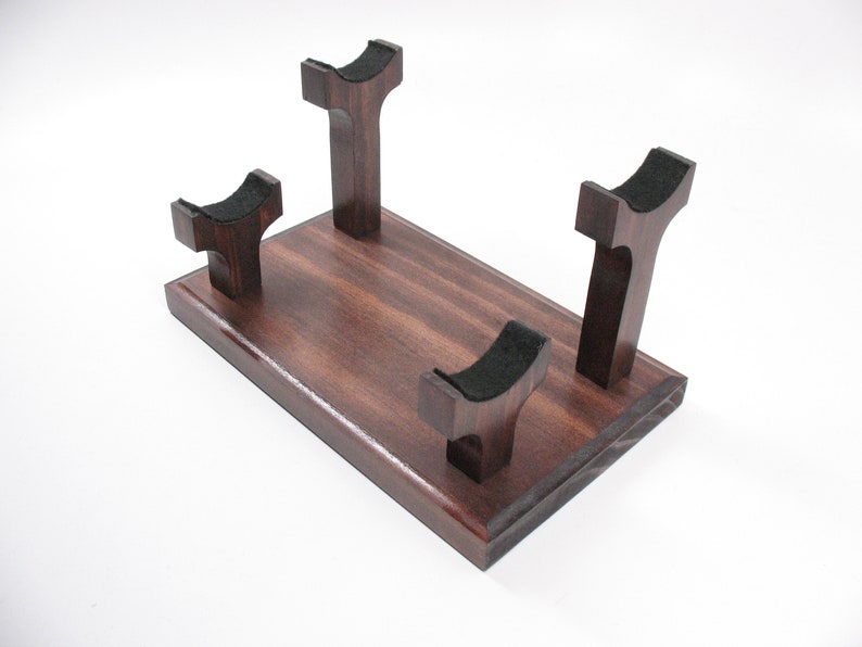 May include: A wooden display stand with a rectangular base and four upright supports. The supports have a curved top with black felt padding. The wood has a rich, dark brown finish.
