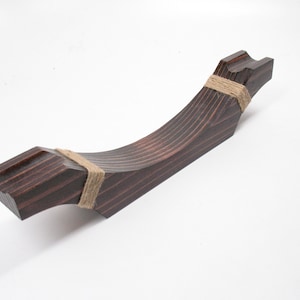 May include: A dark brown, wooden decorative object with a curved, angular design. The object is wrapped with twine at two points. The wood grain is visible, and the object has a smooth, polished finish. The object is likely a decorative piece.